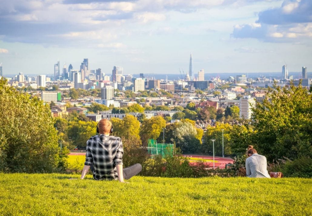 Back view of tourists looking over the London city skyline from Parliament Hill in Hampstead Heath.