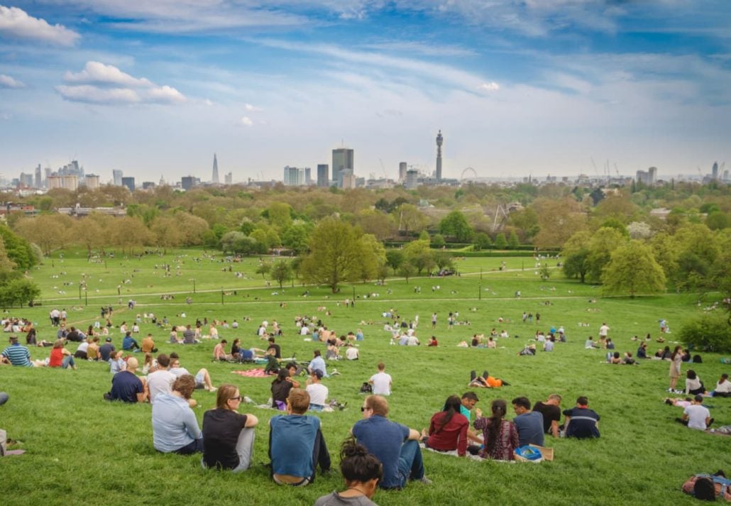 Breath-taking panoramic scenic view of London cityscape seen from a crowded Primrose Hill park on a sunny spring afternoon.