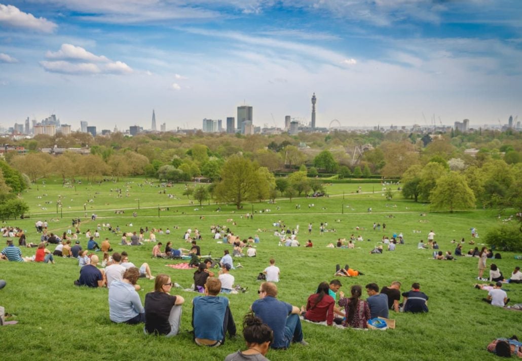 parks-in-london-primrose-hill | CuddlyNest Travel Blog Breath-taking panoramic scenic view of London cityscape seen from a crowded Primrose Hill park on a sunny spring afternoon.
