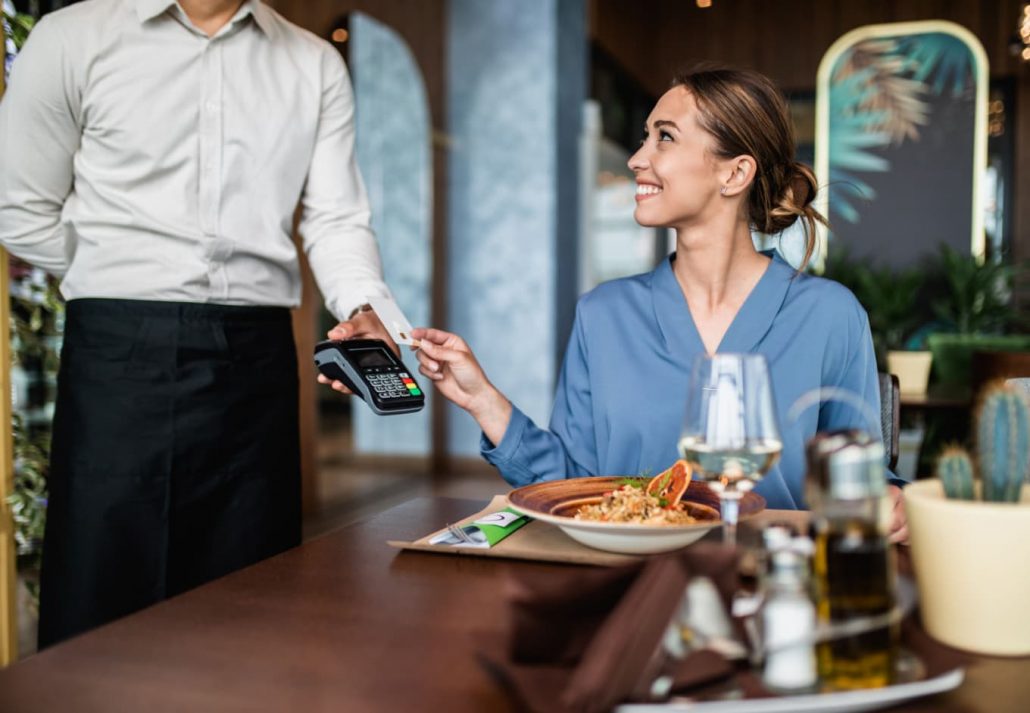 Woman happily paying for her meal at a restaurant with her credit card.