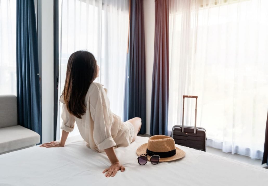 a woman sitting on a bed in a hotel room with luggage in front of her