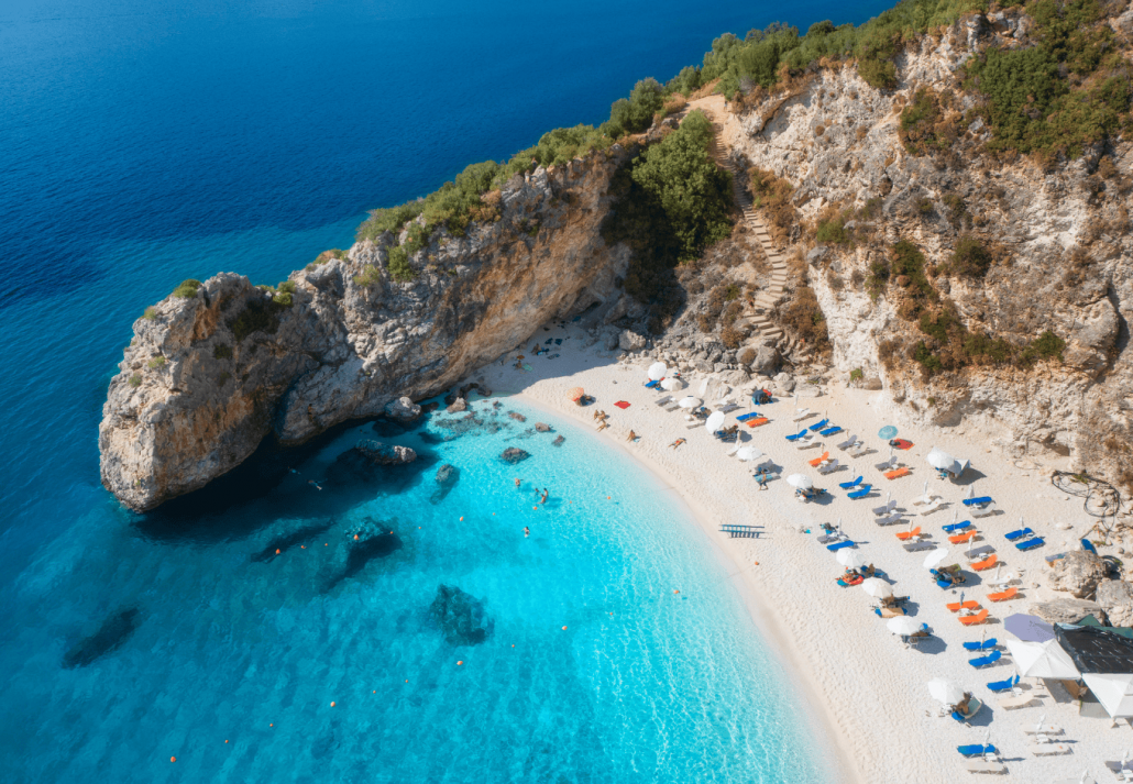 Aerial view of blue sea, rock, sandy beach with umbrellas