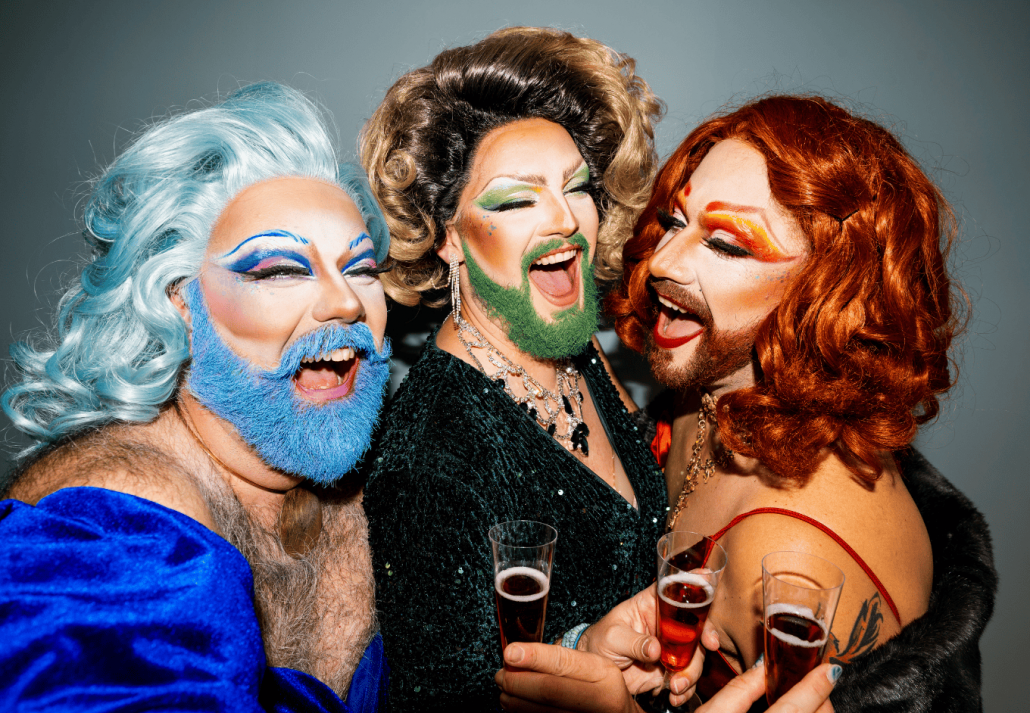 Three drag queens celebrating in style with toasting wine glasses