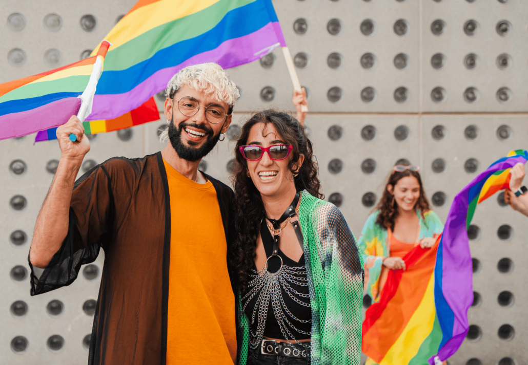 
best lgbtq friendly hotels in the USA Gay young man and lesbian woman celebrating the lgbt pride parade with their friends, waving the rainbow