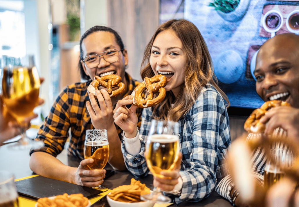 Young multi ethnic people group eat brezel and drinking beer at brewery bar restaurant at happy hour