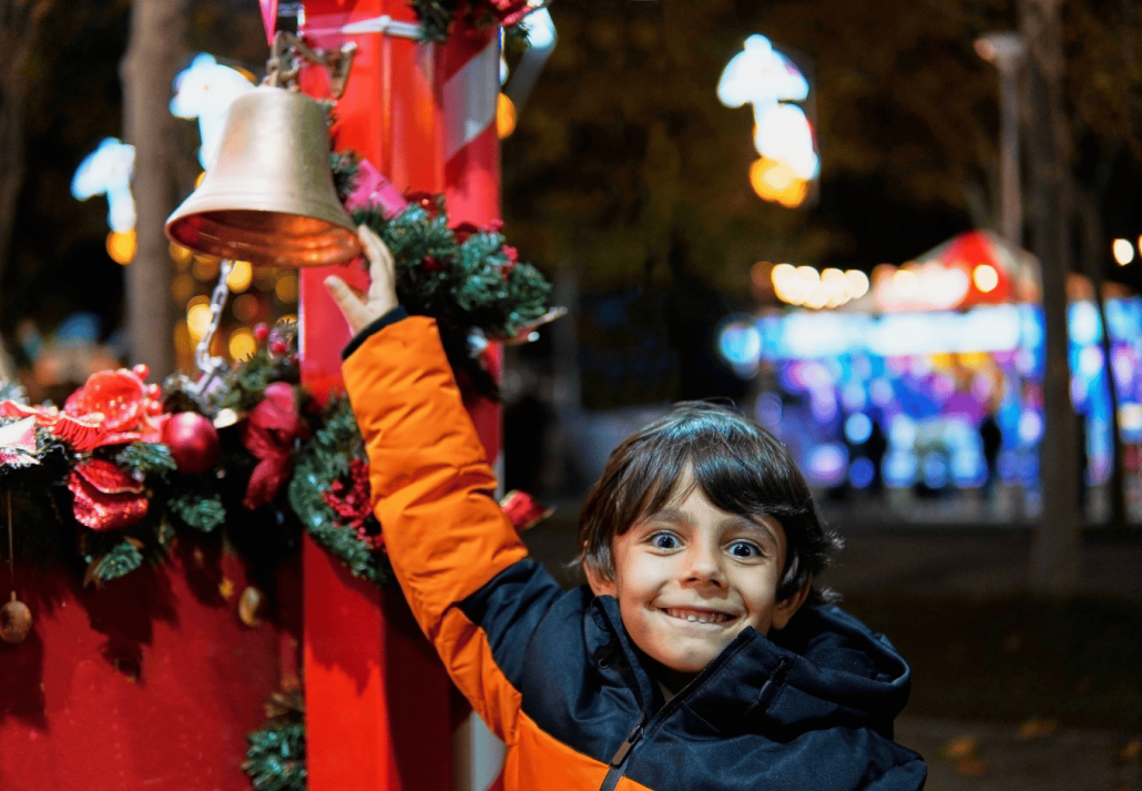 Boy jingling bell at night in a christmas market stall