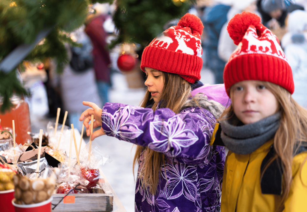 Two children in winter clothes choose homemade sweets at the Christmas market.