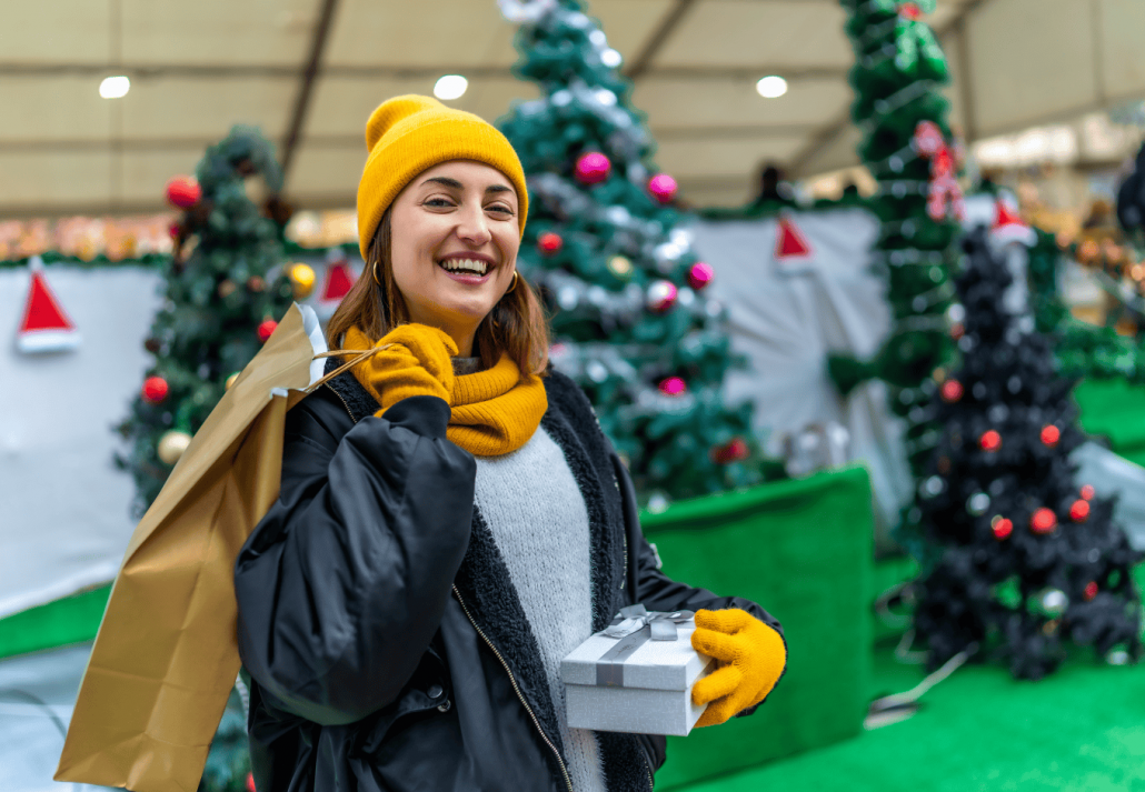 Une femme heureuse tient des sacs à provisions et une boîte cadeau sur le marché de Noël