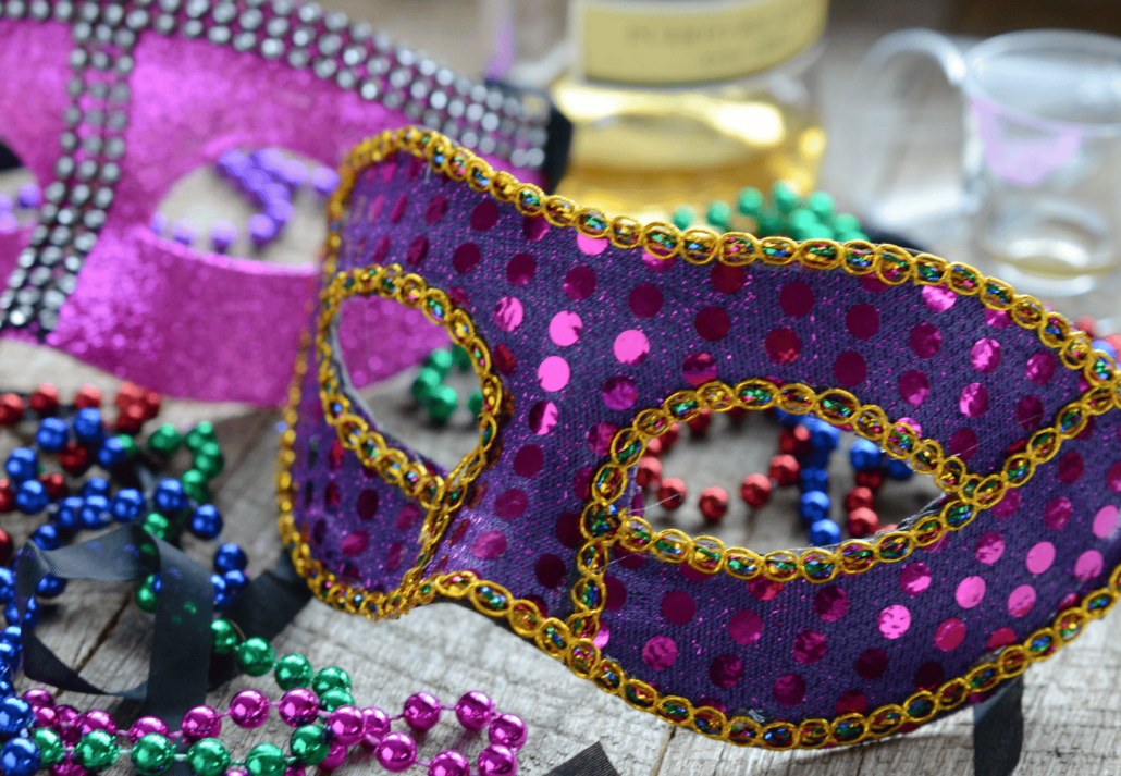 Mardi Gras mask and beads next to liquor bottle and shot glasses - Celebrating Fat Tuesday 