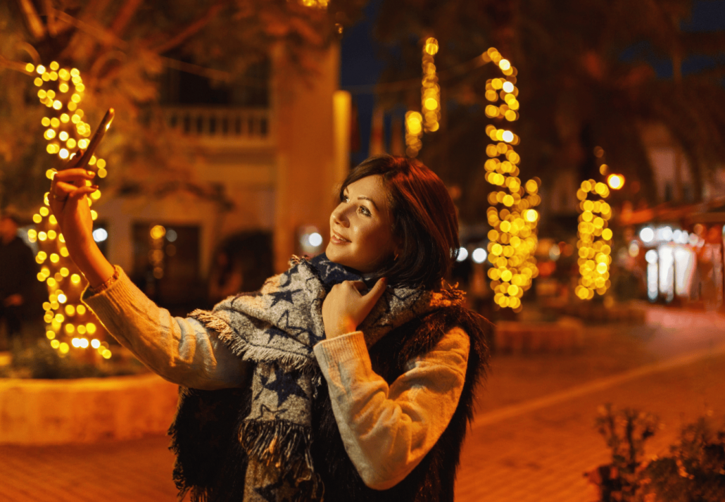 Young woman making selfie in front of Christmas street decorations in city